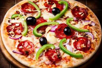 Pizza with chorizo ​​sausage, mozzarella cheese, green pepper and black olives. Rustic wooden background. Soft focus.	