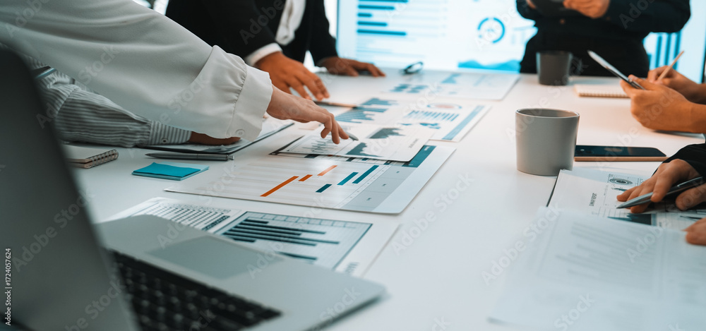 Poster a business team engages in a collaborative meeting, analyzing financial reports and data charts laid