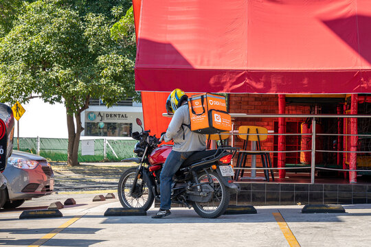 Didi driver food delivery service riding his motorbike with orange box. Sharing collaborative economy concept in South America. Guadalajar, Jalisco, Mexico, December 24, 2024.