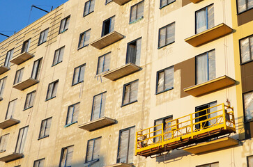 Suspended construction cradle on painting facade of building. Mobile scaffolding platform for construction work at height, facade cleaning, plastering. Insulation and wall painting, cladding.