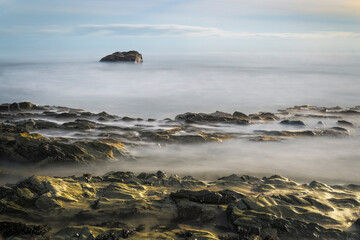 Irish seascape with rugged rocks and solitary stone in misty long exposure sea, tranquil coastal landscape.