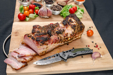 Cropped bacon with knife on wooden cutting board. Spices and vegetables in defocused view. Protein