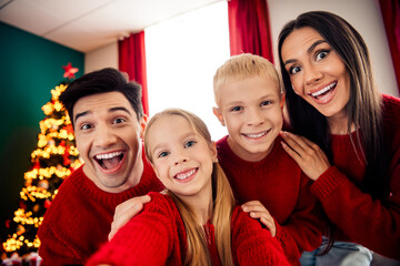 Happy family enjoying Christmas day together indoors, dressed in red sweaters, celebrating by a...