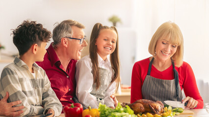 Happy multi generation family with grandparents and grandkids cooking festive Thanksgiving or Christmas meal, preparing yummy turkey for holiday celebration, making dinner together at kitchen