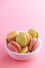 Different flavors of macarons. Colourful macaroons in bowl on pink background.