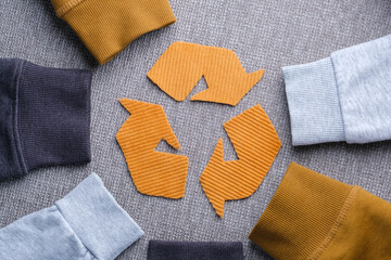 Sweater sleeves in shades of gray, mustard, and light blue surround a recycling symbol made from orange fabric. Concept of clothing recycling, sustainable fashion, and textile waste reduction.