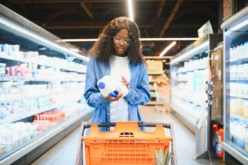African American Woman Taking Milk Bottle, Shopping Groceries In Supermarket On Weekend. Happy...