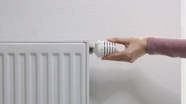 Hand adjusting heating radiator thermostat, showcasing the transition to colder seasons, emphasizing the importance of temperature control for home comfort and energy efficiency