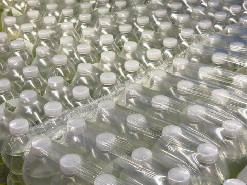 Bulk packaged clear plastic bottles with white caps in rows for distribution - Powered by Adobe