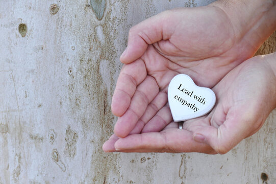 Lead with empathy - man holding in hands white wooden heart with text motivational background