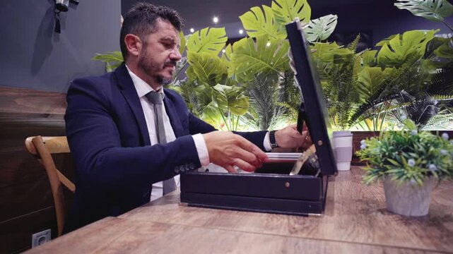 Businessman sitting at a table opening a briefcase