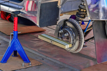 Wheel alignment and camber check on a car, with measuring tool attached to the brake disc and suspension visible during maintenance work.