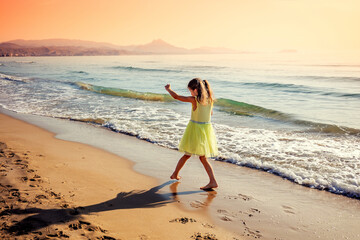 Activity on the beach in summer. Happy little girl runs on the beach. The kid in the yellow dress