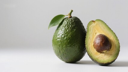 Whole and halved avocado with green skin and pit on a white background