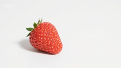 A single ripe strawberry with green leaves on a white background