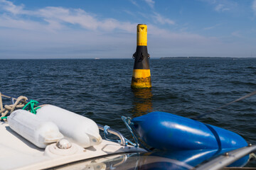 Fototapeta premium View from a yacht's bow of a large yellow and black cardinal navigation buoy in the open blue sea.
