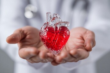 A closeup of a woman's hand holding a glass of red wine and a red heart symbolizing love and celebration