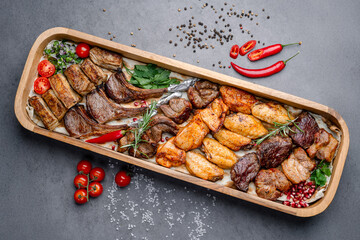 Assorted grilled meat platter with spices. Top view of assorted grilled beef, chicken, lamb, and pork served on a wooden tray with spices and vegetables.