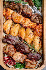 Grilled meat assortment close-up. A wooden tray with grilled chicken wings, beef and lamb garnished with herbs and pomegranate.