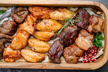 Assorted grilled meat platter. Close-up of roasted chicken wings, beef, and lamb served on a wooden tray with pomegranate and herbs.