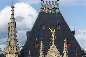 The Provinciaal Hof of Bruges Historic Gothic-style building with ornate stonework, pointed arches, and tall spires a central tower with a statue, and flags above the entrance,