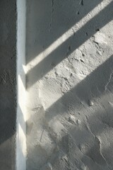 Close-up of a textured plaster wall with diagonal sunlight casting sharp shadows. The interplay of light and surface creates a peaceful, abstract composition evoking calm and simplicity.