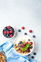 Yogurt with fresh berries and granola on white table.