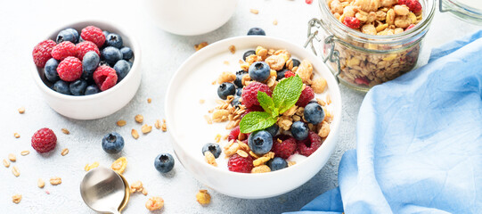 Yogurt with fresh berries and granola on white table.