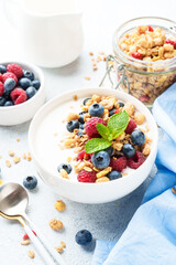 Yogurt with fresh berries and granola on white table.