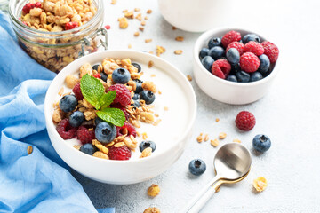 Yogurt with fresh berries and granola on white table.