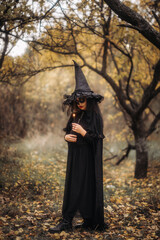 A witch girl with skull makeup holds a candle in a dark forest on Halloween