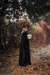 A witch girl with skull makeup holds a candle in a dark forest on Halloween