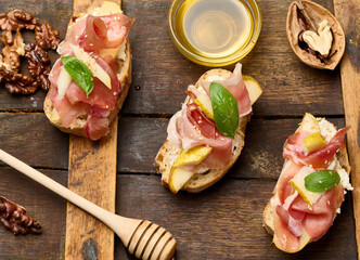Italian bruschetta with prosciutto, pear slices, cream cheese and fresh basil, garnished with sesame seeds, served on a rustic wooden board