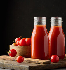 Full glass bottle with tomato juice on dark background