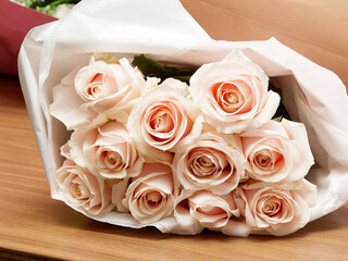 Bouquet élégant de roses pâles roses saumonées, enveloppé dans du papier blanc, posé sur une table en bois, symbole d’amour, de mariage ou de célébration