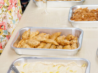 Plateau de samoussas frits servis dans une barquette aluminium lors d’un buffet traiteur oriental, avec houmous et autres mezzés libanais en arrière-plan