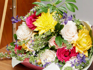 Bouquet coloré de fleurs fraîches avec roses blanches et roses, dahlias jaunes, fleurs violettes et feuillage vert, composition florale élégante posée sur une table en bois