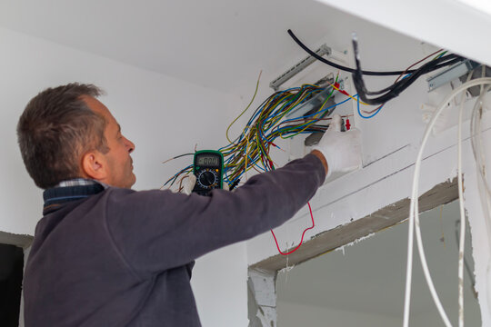 Electrician engineer using a multimeter to test the electrical installation. Man electrician performs installation work. Electrical upgrade, improvement of home.