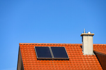 Solarthermie - Warmwassererzeugung -Flachkollektoranlage auf rotem Ziegeldach umrahmt mit grünen Bäumen