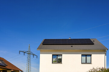 Solaranlage auf modernem Einfamilienhaus vor blauem Himmel und Strommast