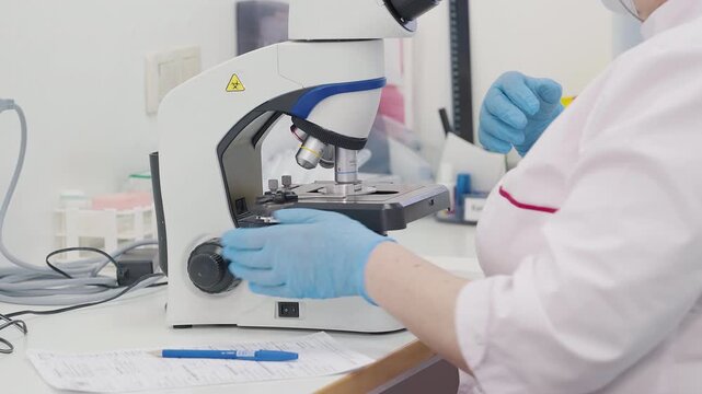 Microscope Used By Scientist To Diagnose Disease. Scientist Analyzing Blood Smear Under Microscope. Checking Blood Sample For Disease. Scientist Writes Disease Examination Result. Optical Microscope