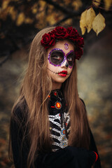 Witch with skull makeup in a dark forest on Halloween.
