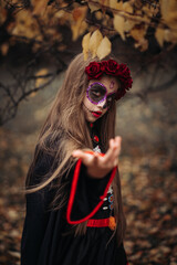 Witch with skull makeup in a dark forest on Halloween.
