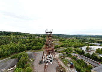 Rusty abandoned industrial tower rising above green forest landscape, captured from aerial view....