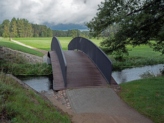 A new arched wooden bridge across a small river. Summer season.
