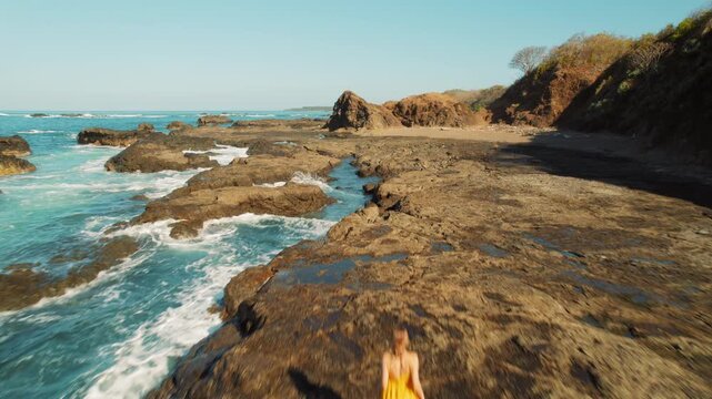 Woman walks on rocky coastline with ocean waves at San Juanillo beach Costa Rica