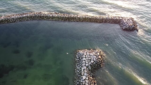 Aerial view of sturdy piers and wave breakers at Lausanne, protecting the calm waters of Lake Geneva. The stone structures gleam under the sunlight against the gentle waves.