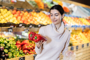 Young woman buyer choosing fresh bell peppers in vegetable shop