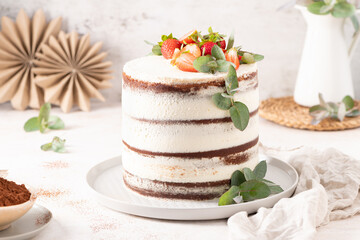 Striking naked cake with layers of rich chocolate and vanilla cream, elegantly topped with fresh strawberries and eucalyptus