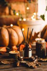 Aroma reed diffuser, pumpkins, knitted warm sweaters, candles, dry leaves on wooden table. Concept of house decor, apartment seasonal fragrance. Thanksgiving. Autumn mood, cozy fall home atmosphere